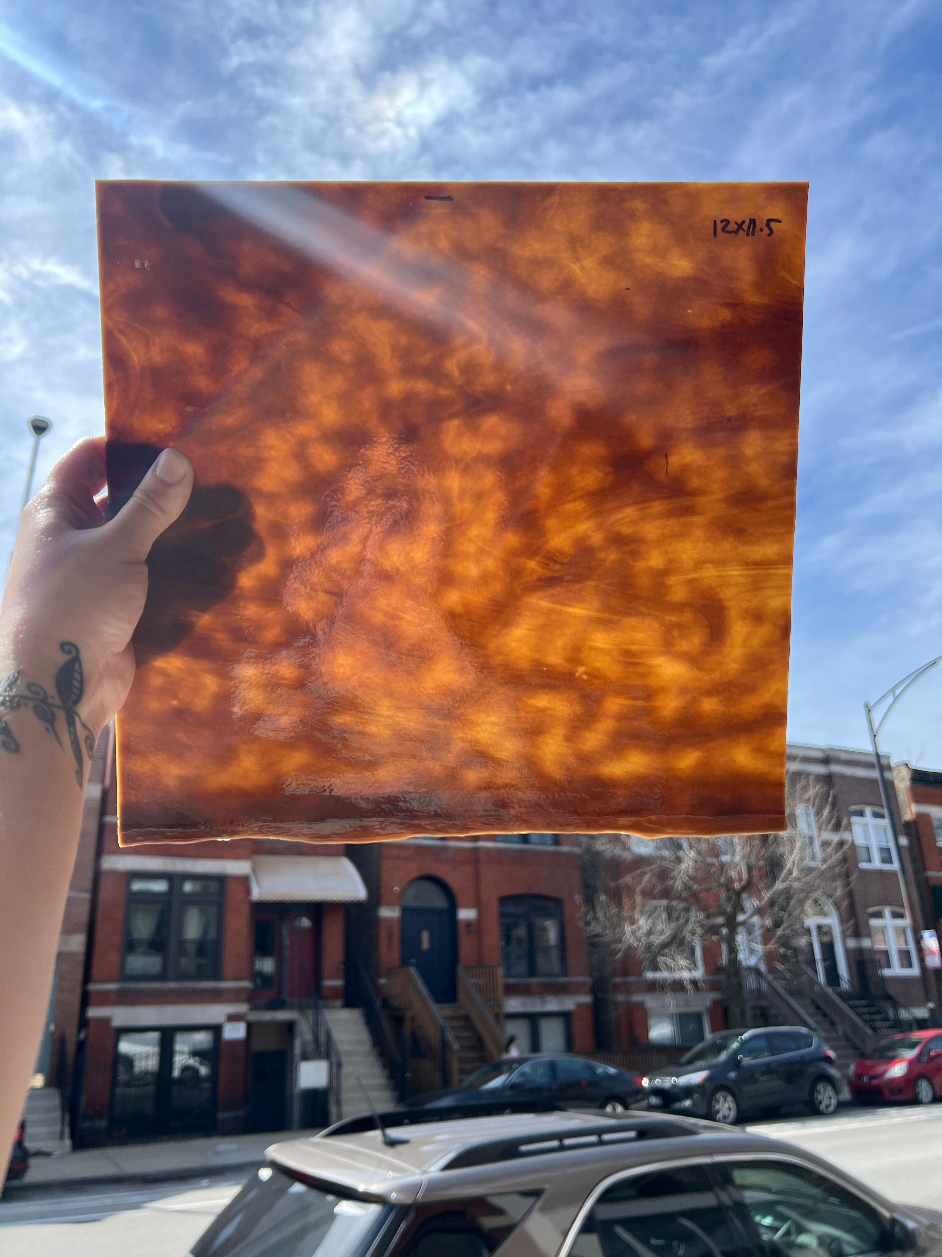 Person holding a rust colored piece of glass with urban street scene in the background