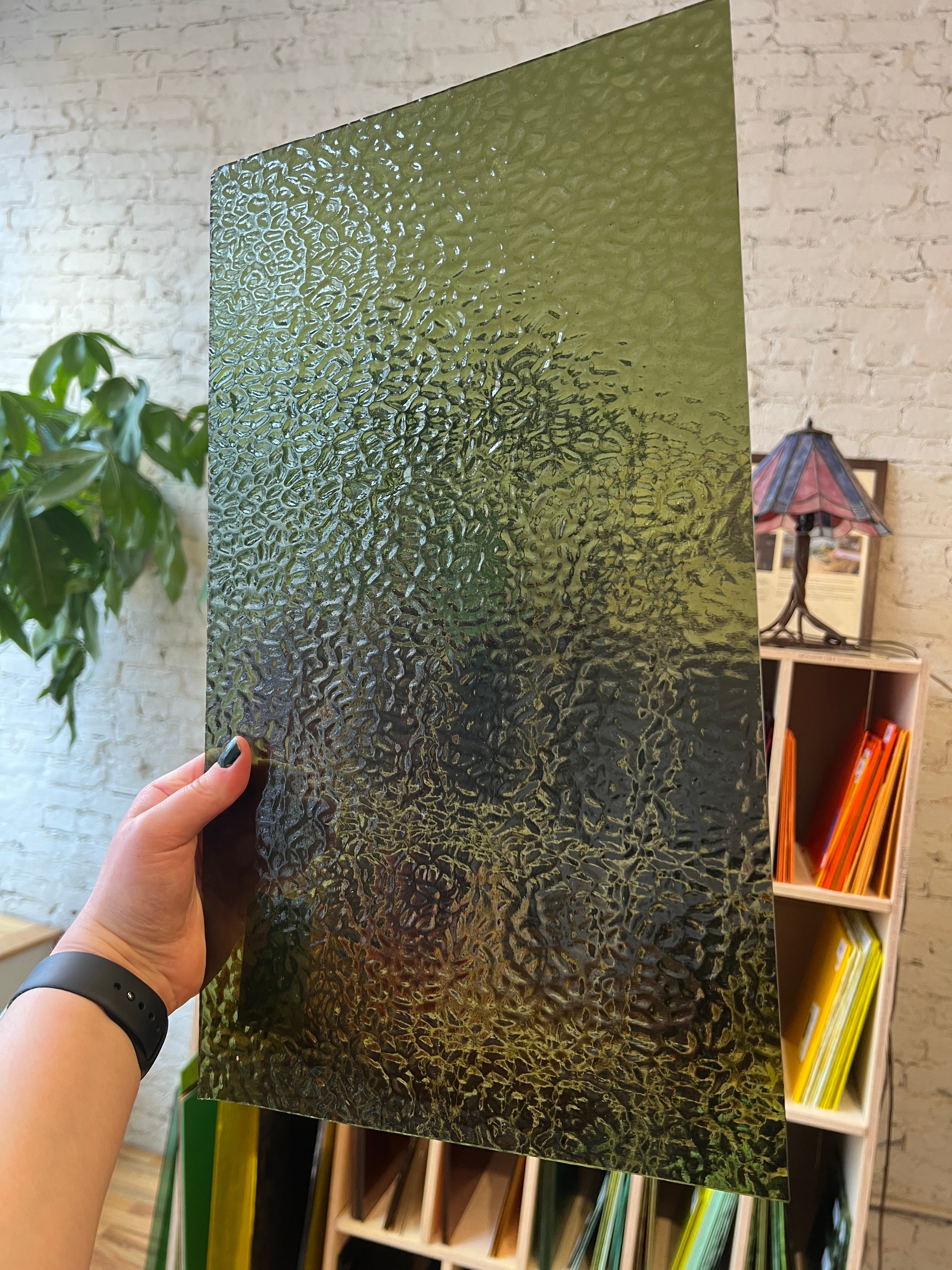 Hand holding a textured green piece of glass with shelves in the background