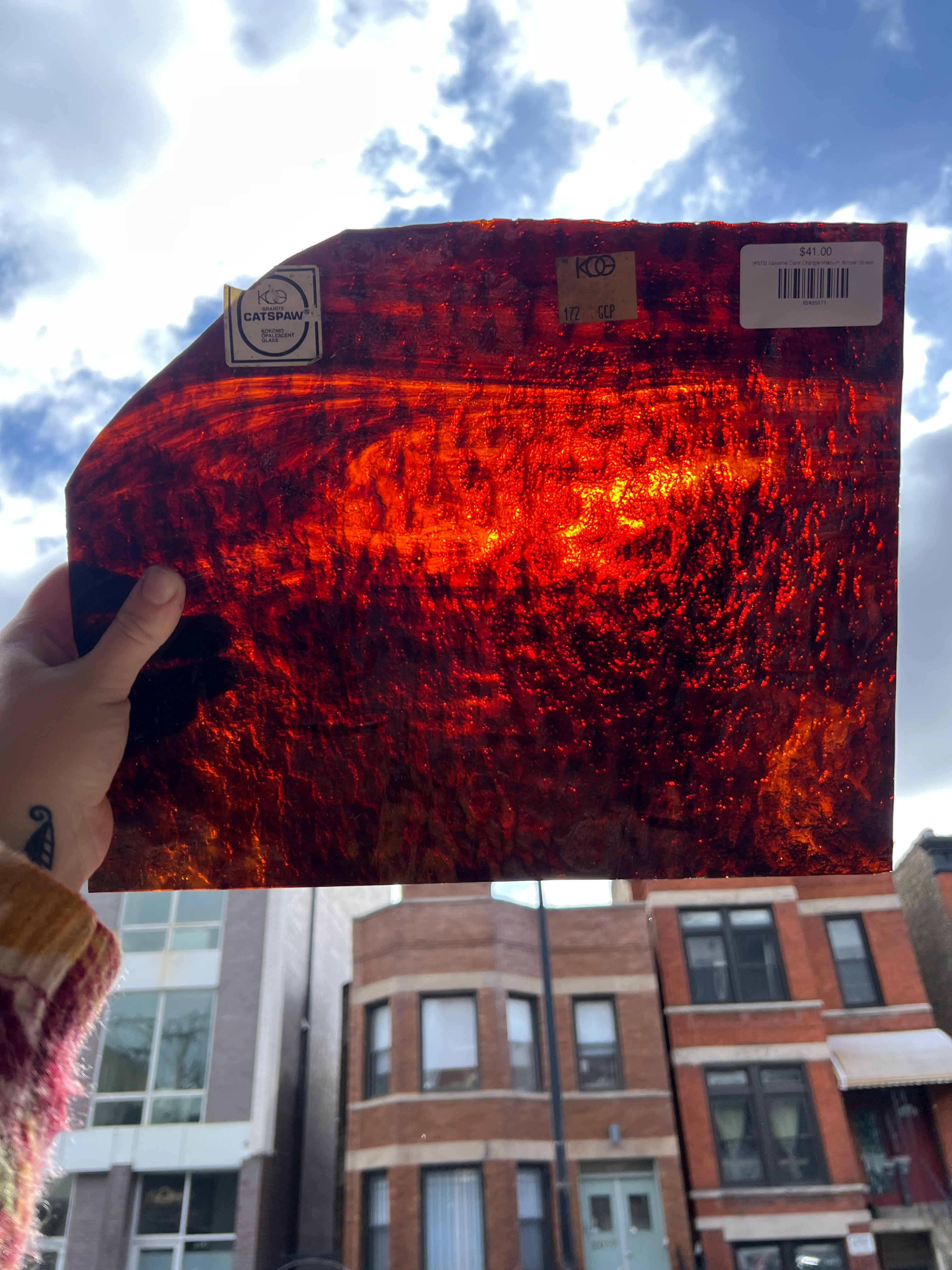 Person holding a piece of red mottled stained glass against a cityscape background