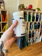 Hand holding a cylindrical container with black and white labels in an art supply store.
