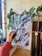 Person holding a piece of abstract stained glass with a plant and bookshelf in the background