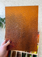 Hand holding a textured brown sheet of stained glass against a light background