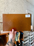 Brown textured piece of stained glass held by a hand on a light background