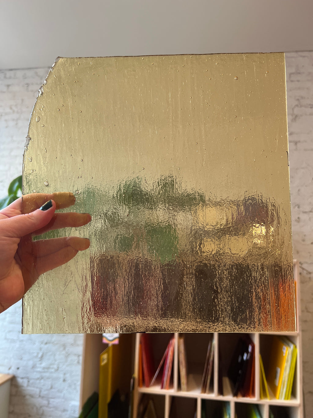 Hand holding a gold-colored piece of glass with a textured surface