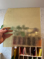Hand holding a gold-colored piece of glass with a textured surface