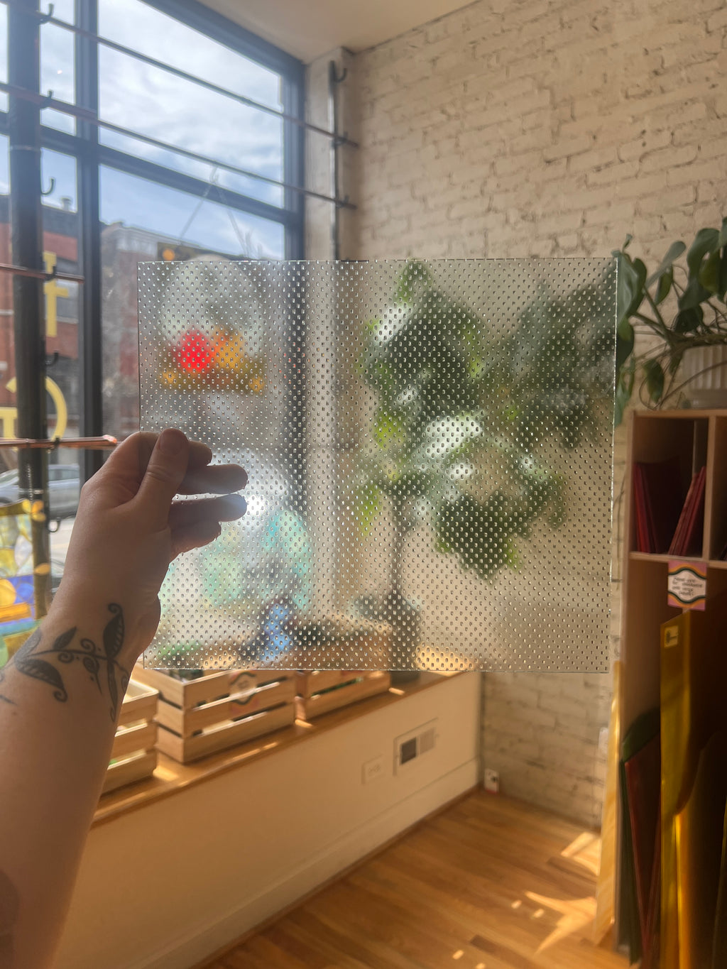 Hand holding a transparent textured sheet of glass against a window with a view of a street.