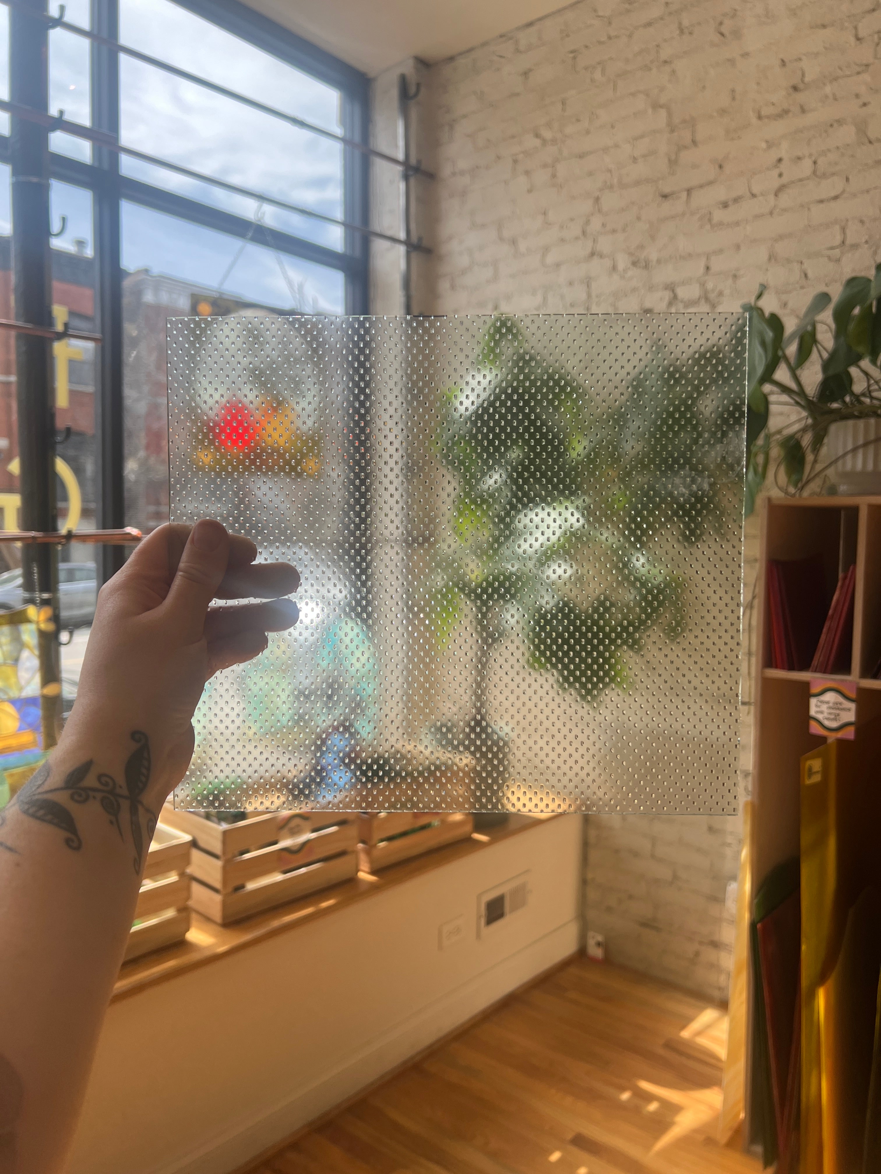 Hand holding a transparent textured sheet of glass against a window with a view of a street.