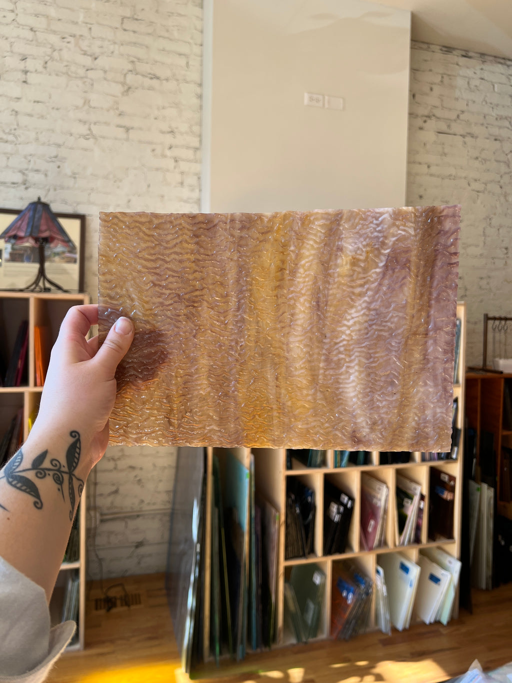 Person holding a brown swirled textured piece of stained glass in front of a blurred sunny interior. 