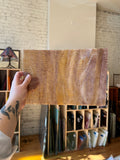 Person holding a brown swirled textured piece of stained glass in front of a blurred sunny interior. 