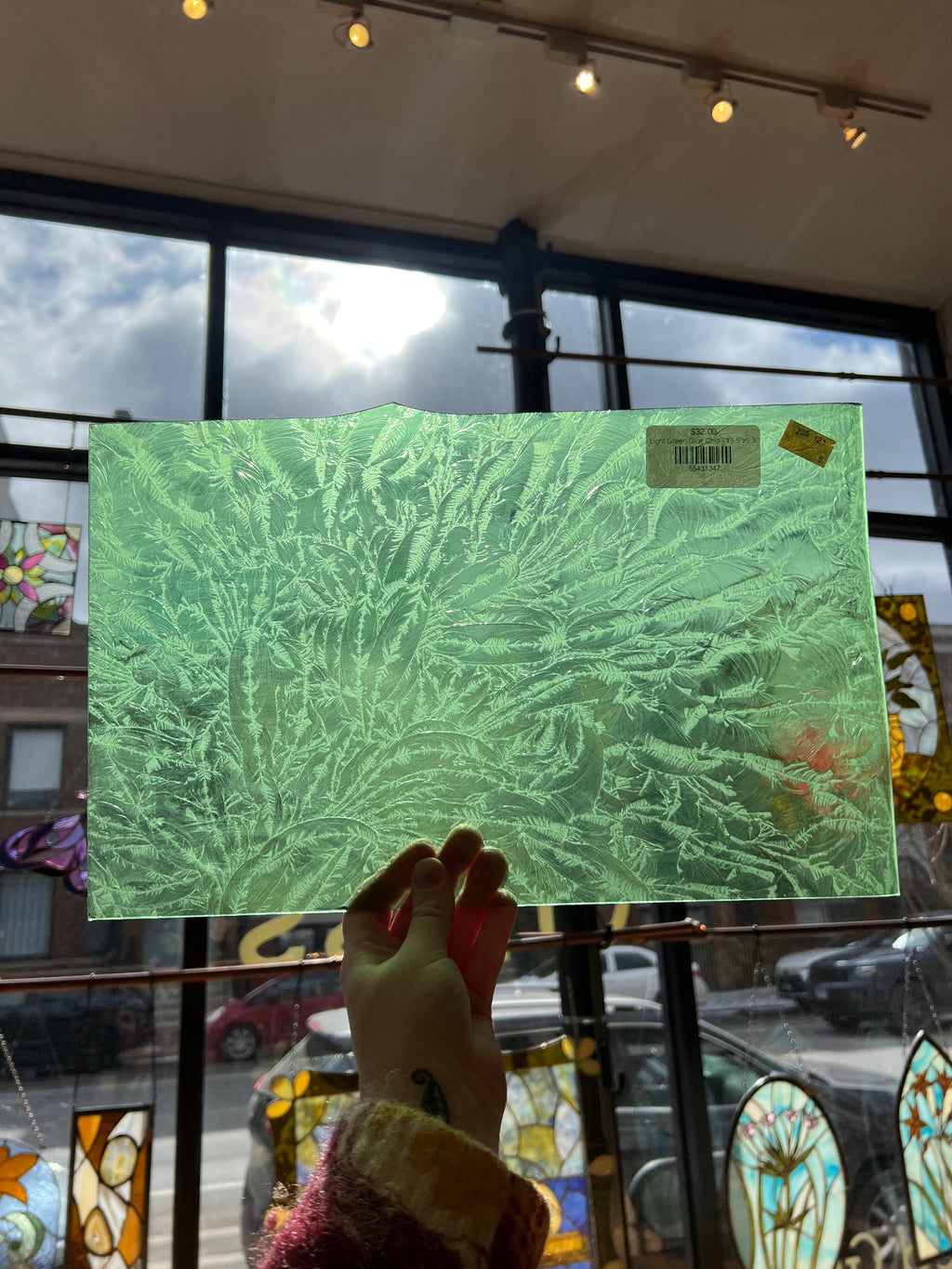 Green textured piece of stained glass held by a hand with stained glass windows in the background