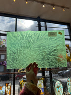 Green textured piece of stained glass held by a hand with stained glass windows in the background