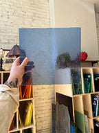Person holding a textured blue sheet of glass in front of a display of colorful shelves.