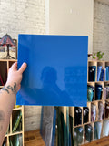 Blue sheet of stained glass held by a hand with tattoos on a neutral background