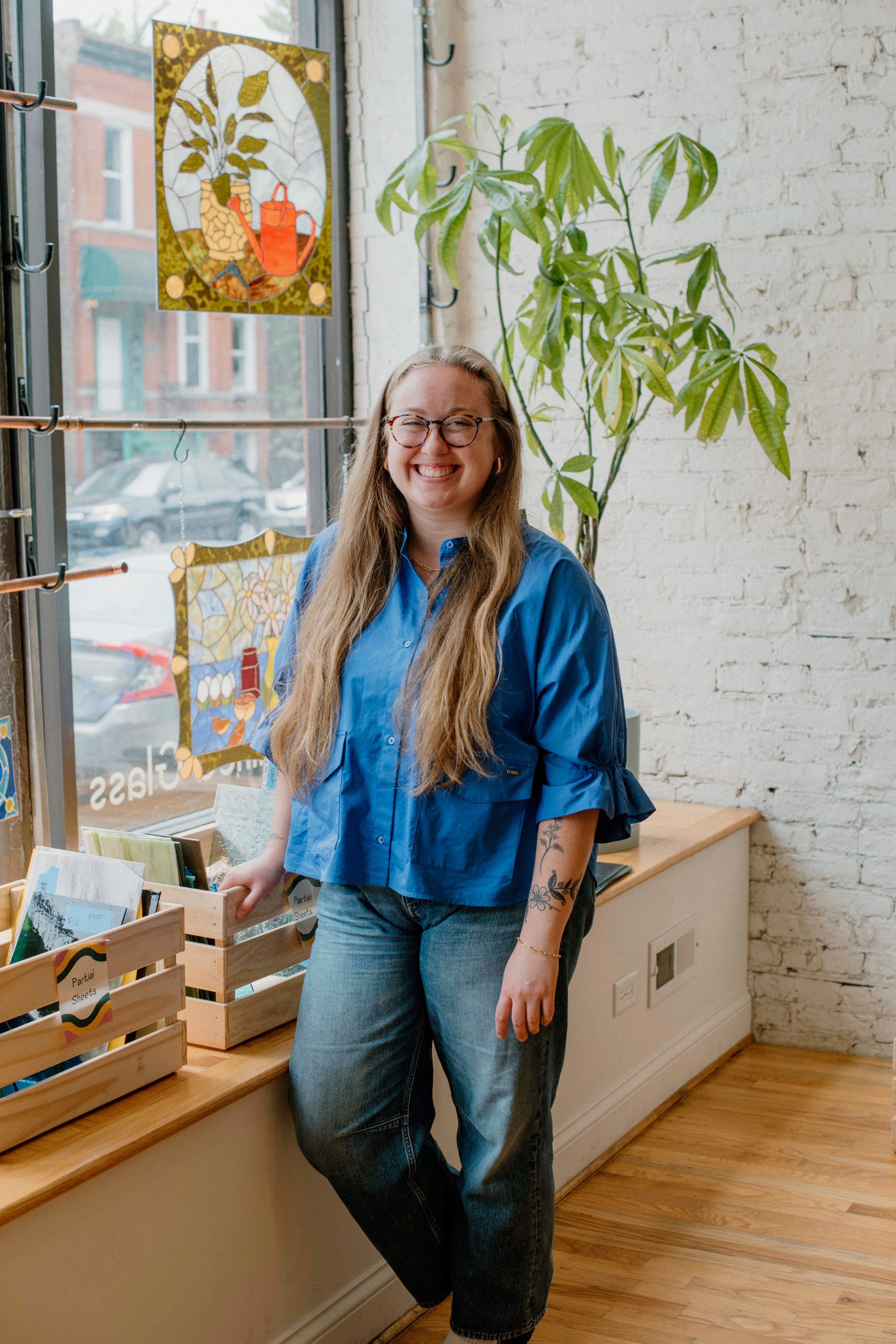 Person wearing a blue shirt standing in a room with a plant and window.