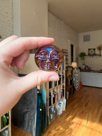 Hand holding an iridescent moon face shaped jewel in an indoor setting.