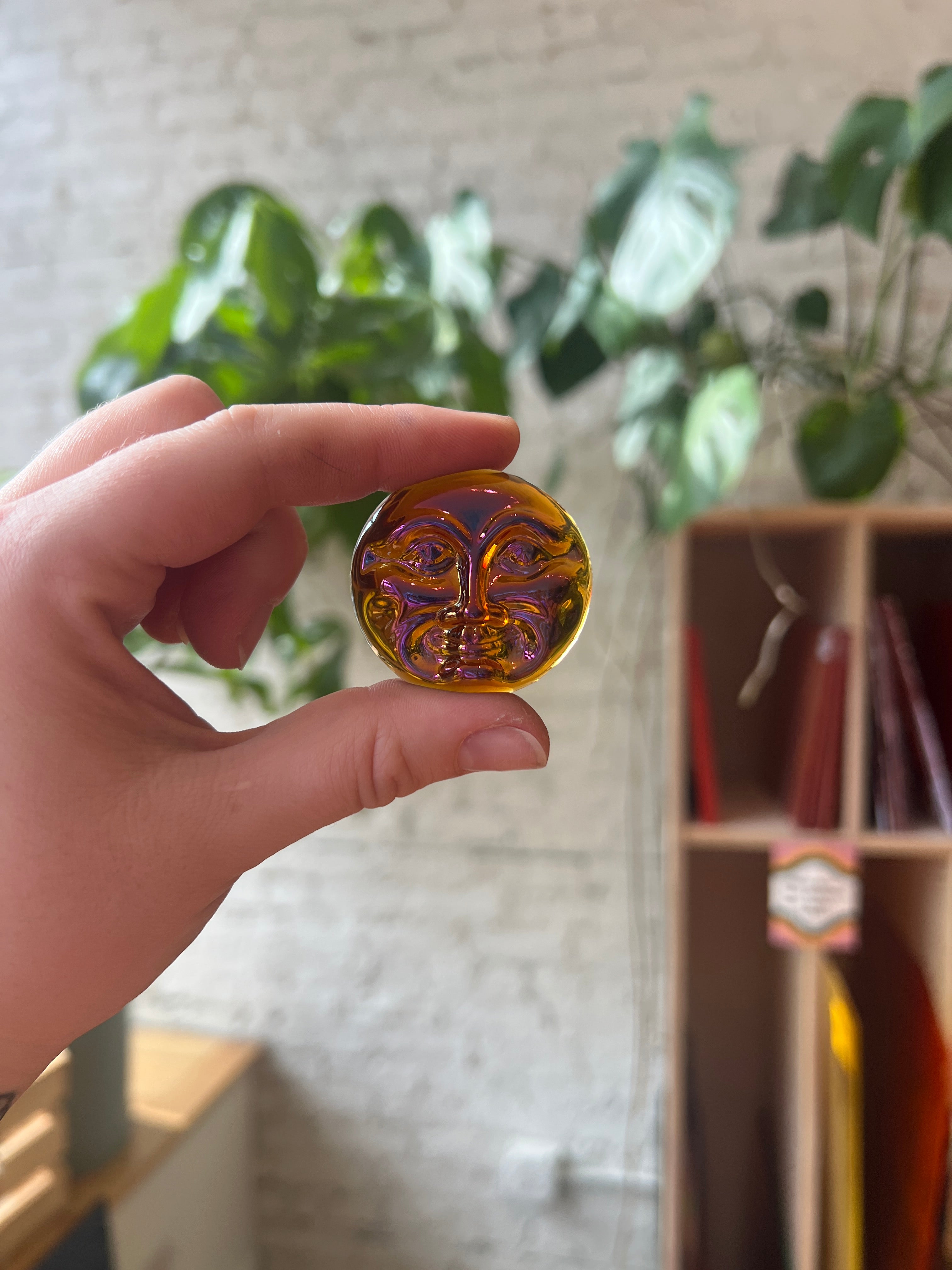 Hand holding a decorative moon face shaped jewel with intricate design, blurred background