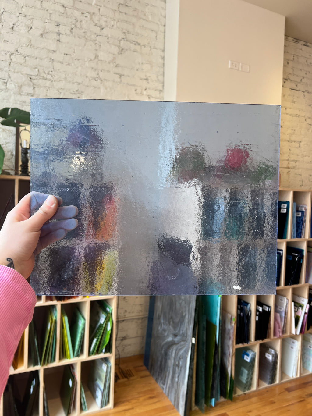 Light blue textured and transparent sheet of glass held by a hand with a bookshelf in the background