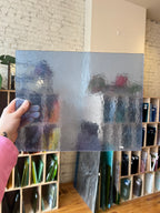 Light blue textured and transparent sheet of glass held by a hand with a bookshelf in the background