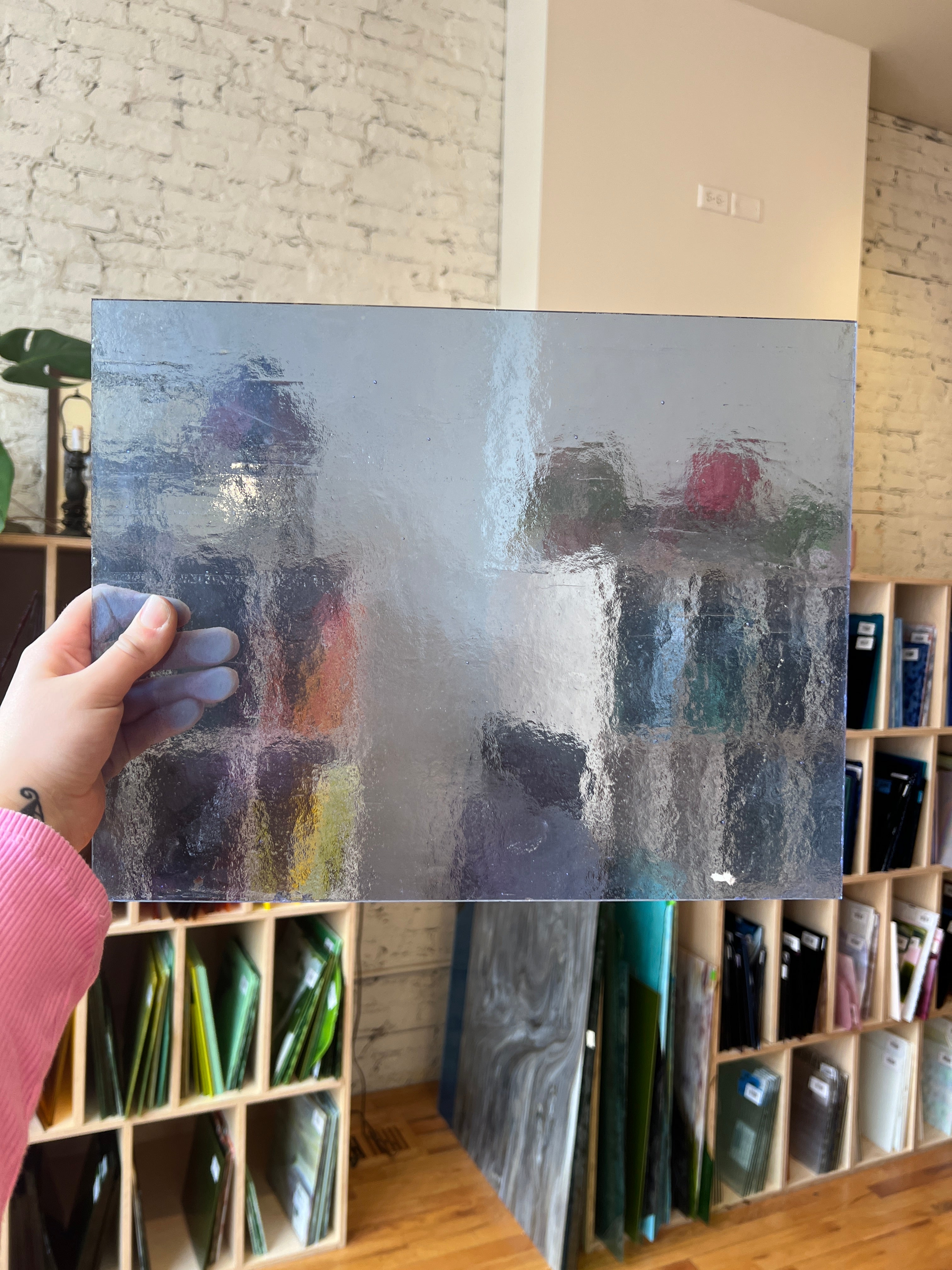 Light blue textured and transparent sheet of glass held by a hand with a bookshelf in the background
