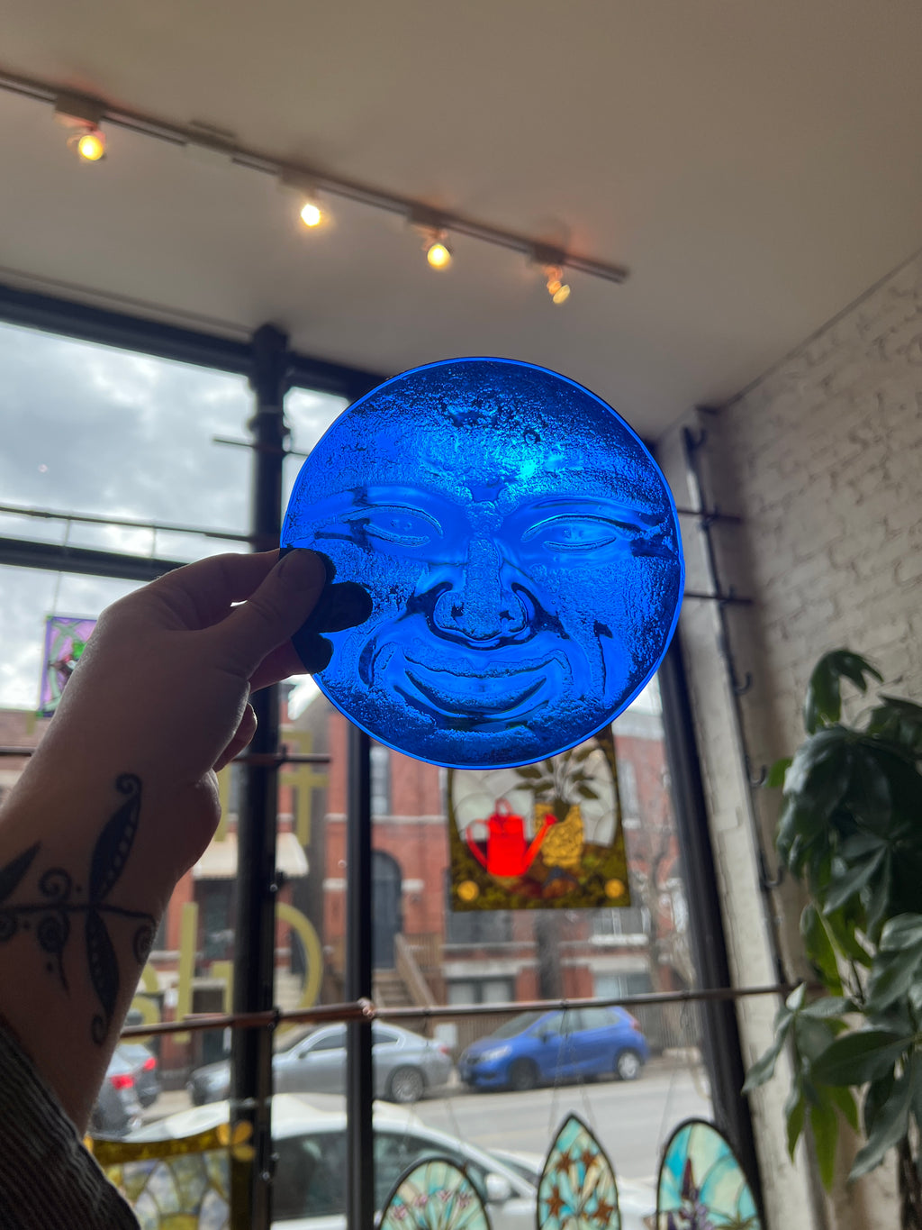 Blue glass moon face held in front of a window with stained glass