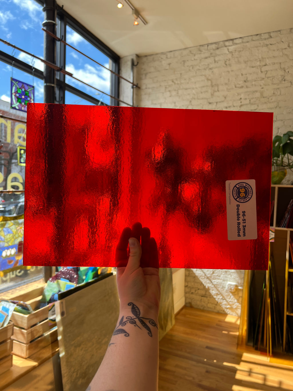 Person holding a red rectangular sheet of stained glass with a logo in an indoor setting