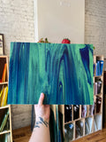 Hand holding a blue and green swirled piece of glass with a blurred background