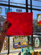 Red piece of stained glass held up in front of a stained glass window display