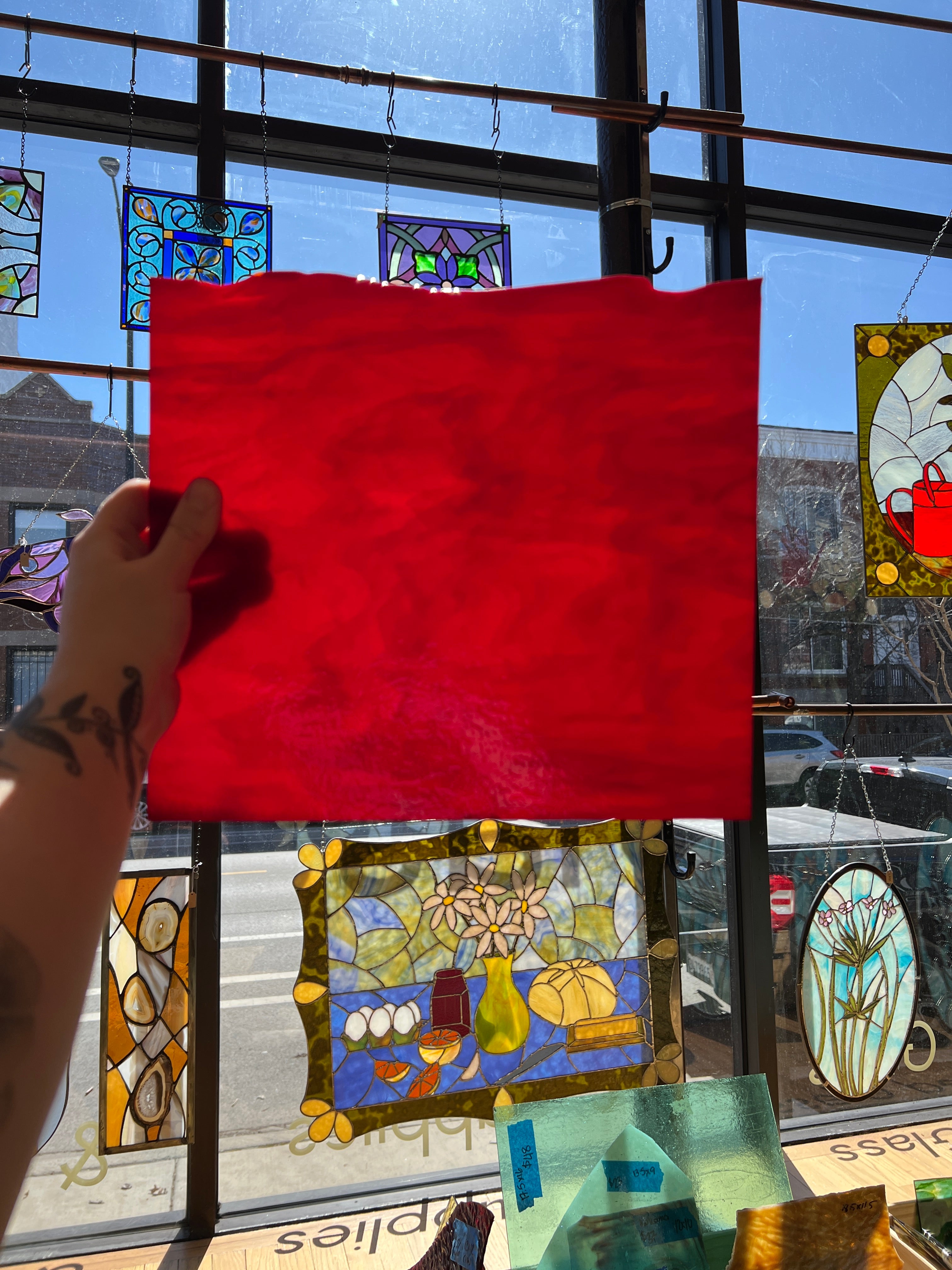 Red piece of stained glass held up in front of a stained glass window display