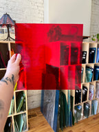 Hand holding a piece of red transparent stained glass in an indoor space.