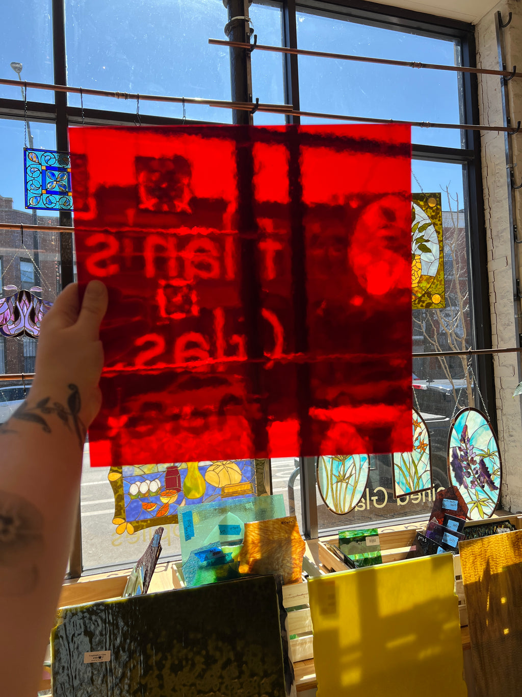 Hand holding a red piece of glass in front of a stained glass window.