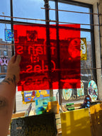 Hand holding a red piece of glass in front of a stained glass window.