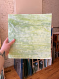 Hand holding a piece of green textured glass with a blurred indoor background