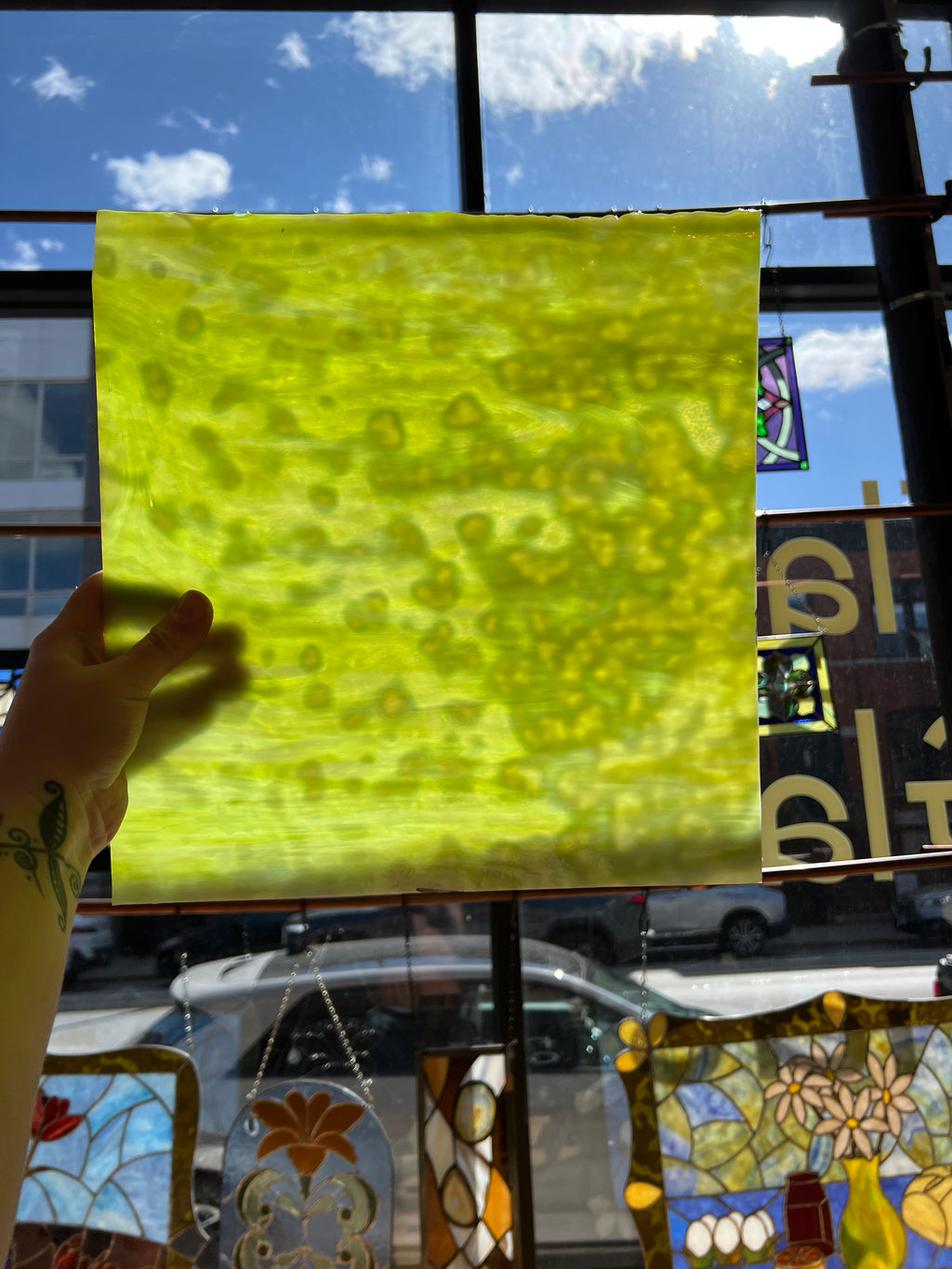Yellowish green mottled piece of glass with a pattern held up in front of a stained glass window