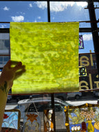 Yellowish green mottled piece of glass with a pattern held up in front of a stained glass window