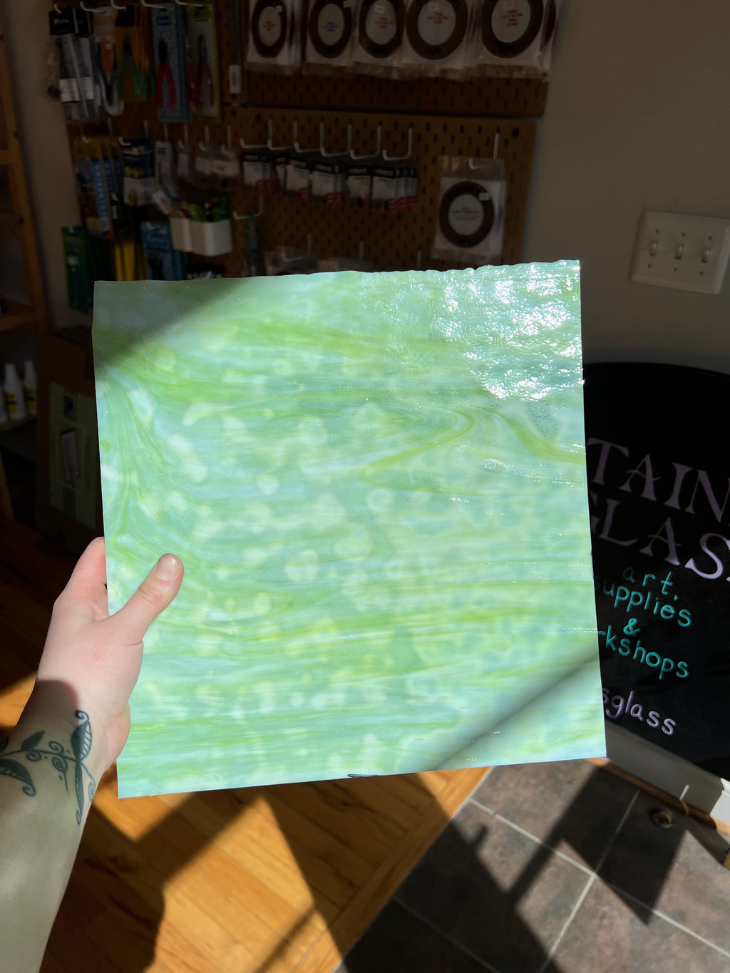 Hand holding a piece of green textured glass in a workshop setting