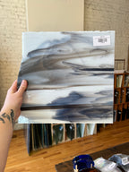 Hand holding a piece of gray and white stained glass with a blurred background