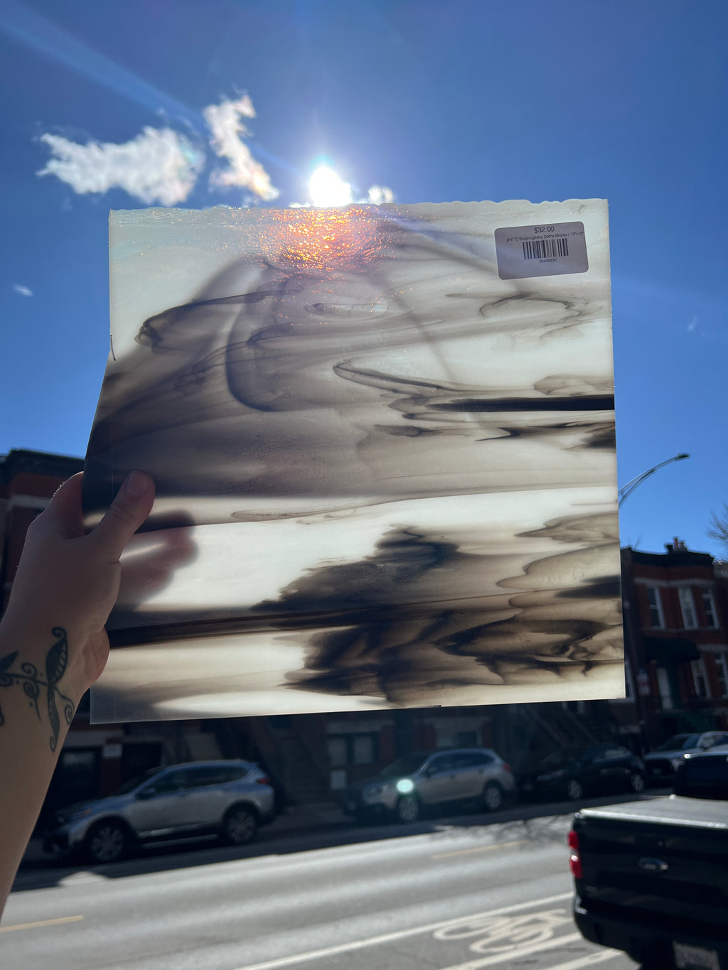 Person holding a piece of stained glass with a black and white abstract design against a blue sky.