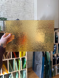 Hand holding a textured gold piece of glass with a background of glass samples