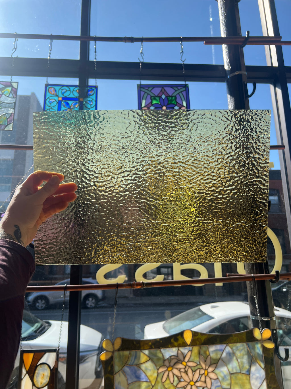 Hand holding a textured glass panel with stained glass windows in the background