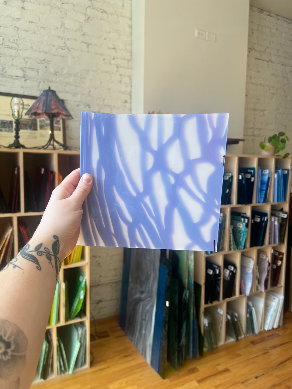 Hand holding a blue and white patterned piece of stained glass in front of a bookshelf.