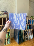Hand holding a blue and white patterned piece of stained glass in front of a bookshelf.