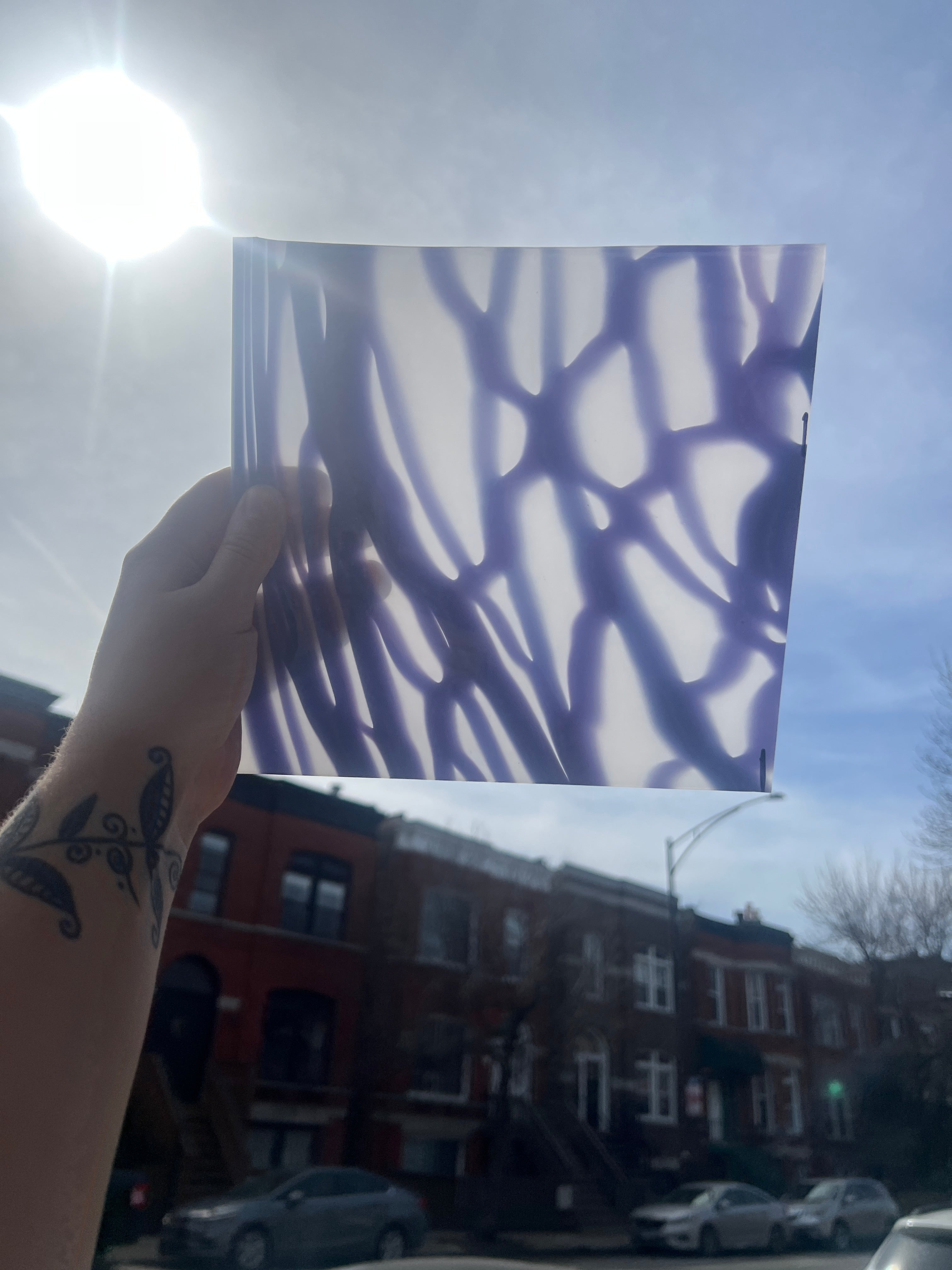 Hand holding a piece of glass with a purple pattern against a city street background