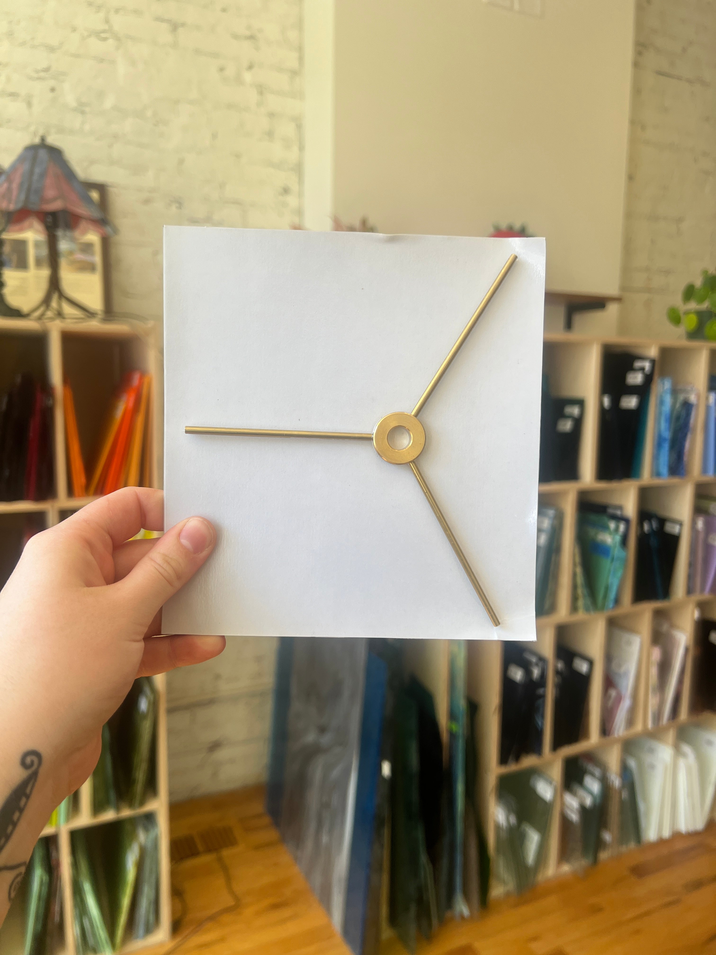 White card with gold lamp piece held by a hand in front of a shelf. 