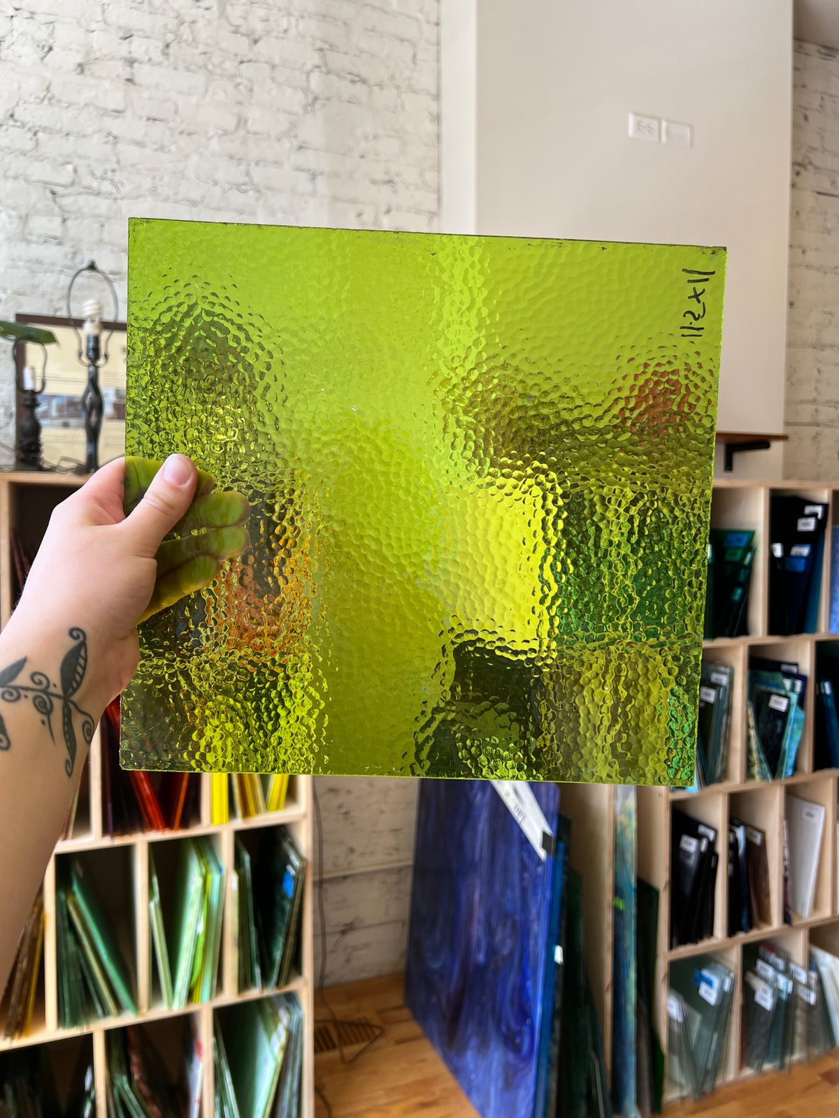 Green textured sheet of glass held by a hand with tattoos, surrounded by various color swatches.