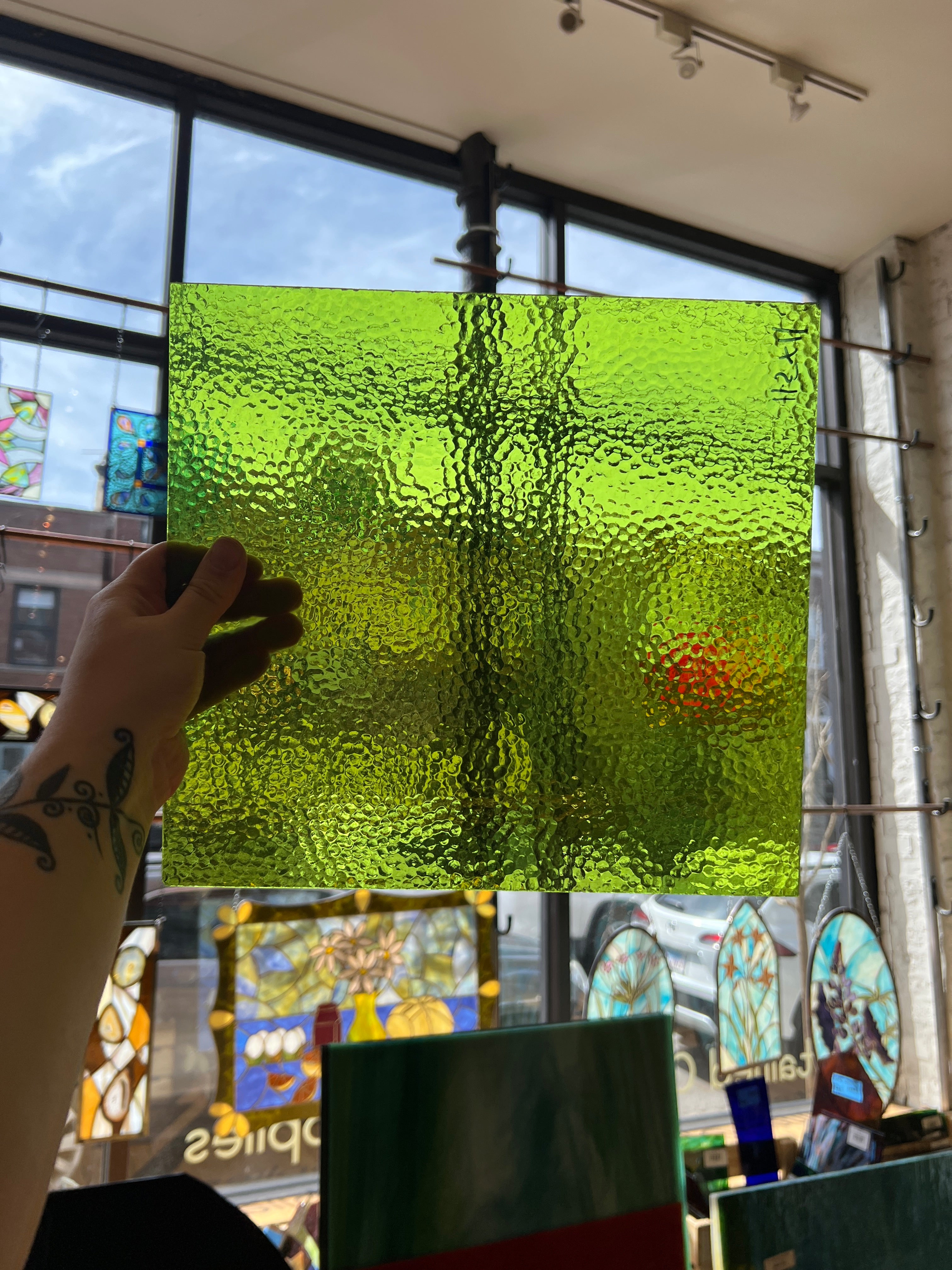 Hand holding a textured green glass panel with stained glass windows in the background