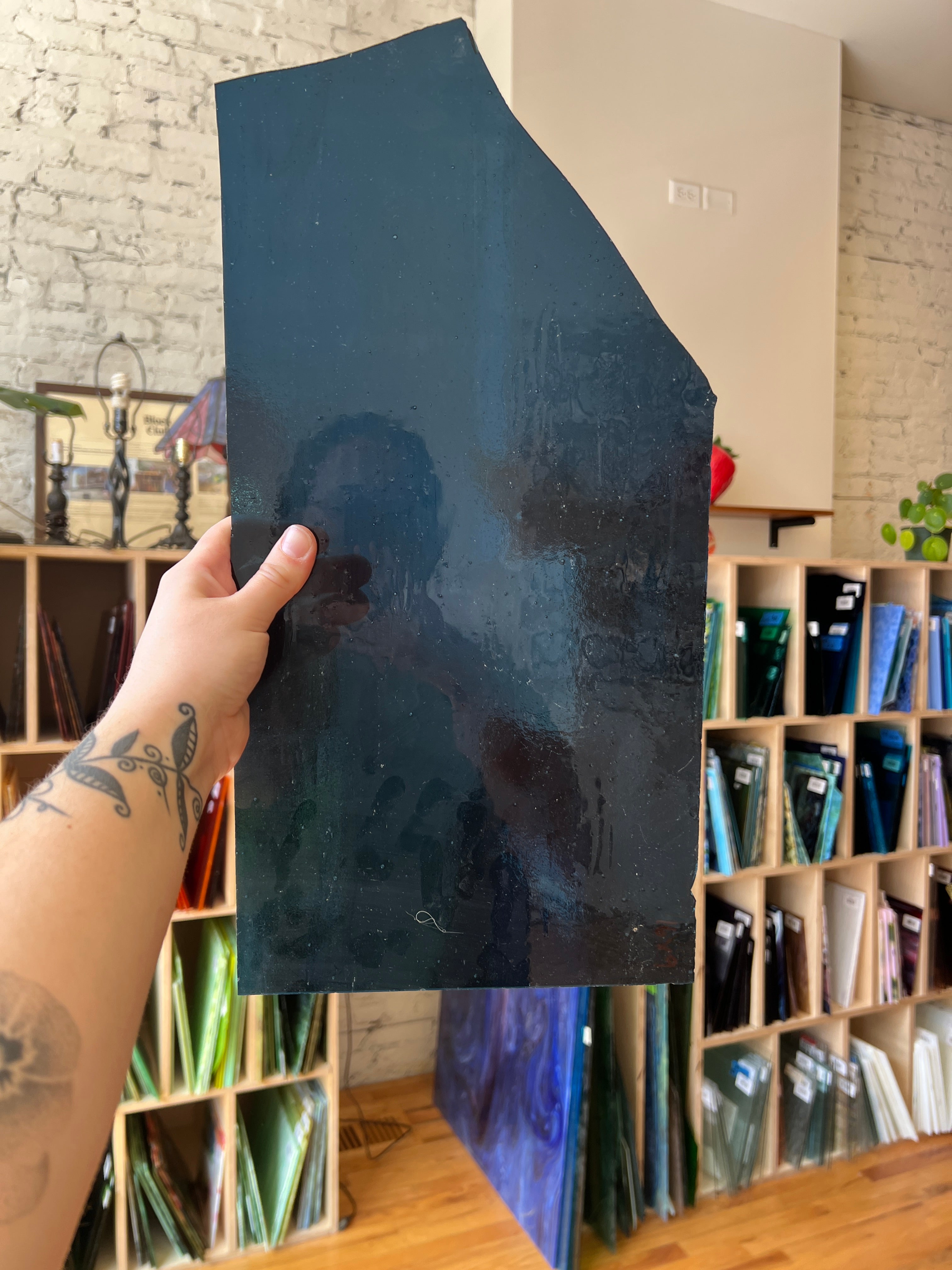 Person holding a dark blue rectangular piece of glass with a blurred background of shelves.