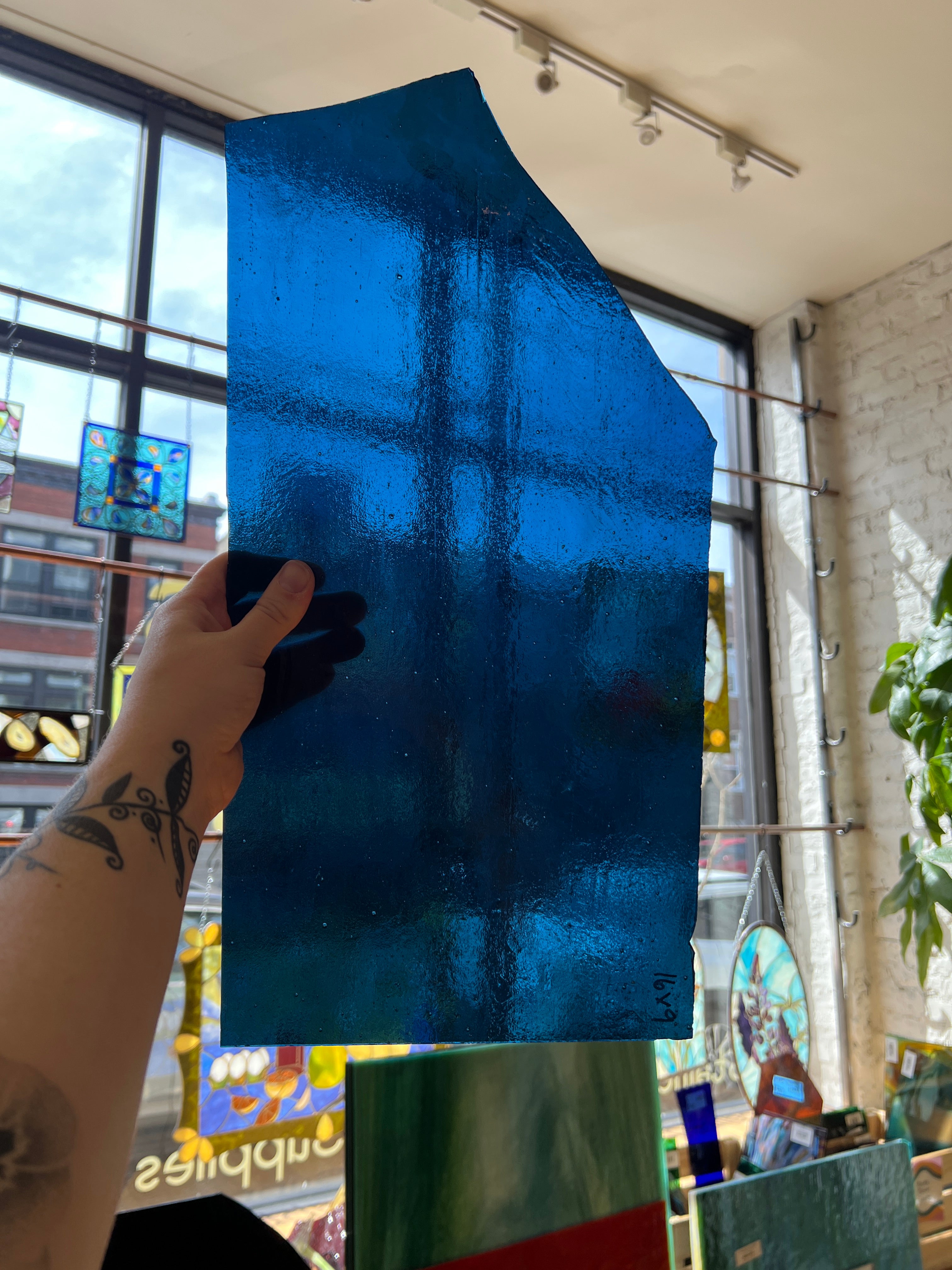 Hand holding a blue piece of glass with a blurred background