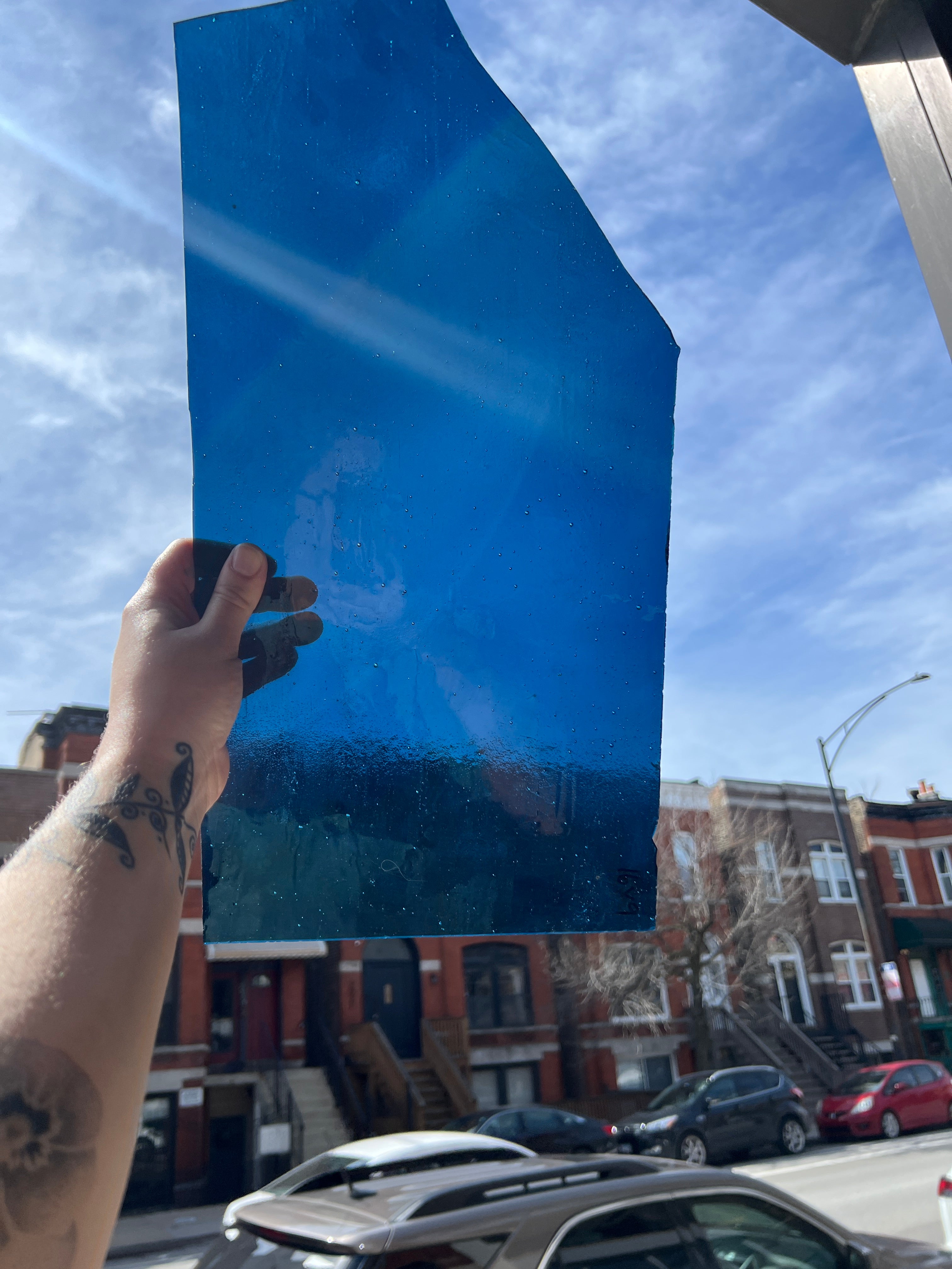 Hand holding a large blue sheet of glass against a city street background