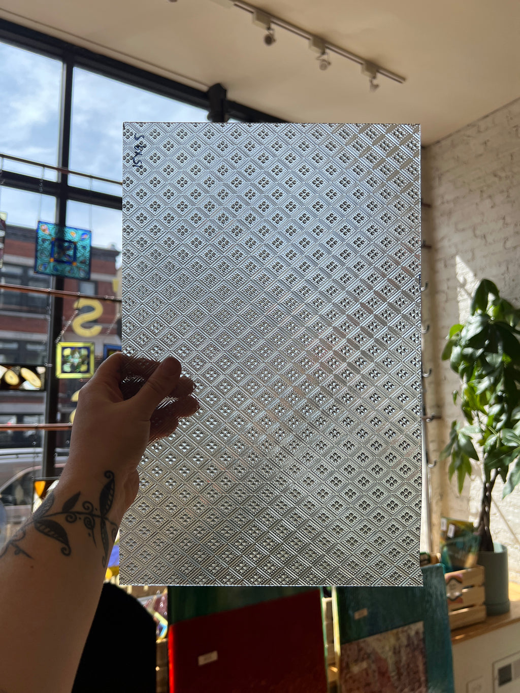Hand holding a patterned sheet of glass against a blurred indoor background