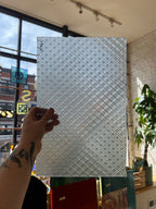 Hand holding a patterned sheet of glass against a blurred indoor background